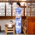 Woman wearing floor-length blue-and-white porcelain floral qipao in traditional setting