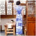 Woman wearing floor-length blue-and-white porcelain floral qipao in traditional setting